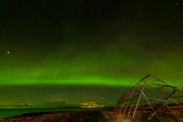 Polarlichter über den Trocknungsgestellen für Fisch in Ekkerøy mit aufgehendem Mond